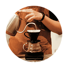 Barista brewing pour over coffee with a stainless steel gooseneck kettle and glass coffee dripper for a handcrafted specialty coffee experience.