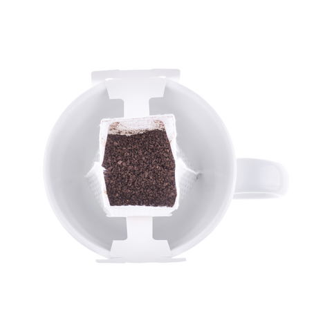 Single-serve coffee drip bag filled with freshly ground coffee placed over a white mug, ready for pour over brewing.
