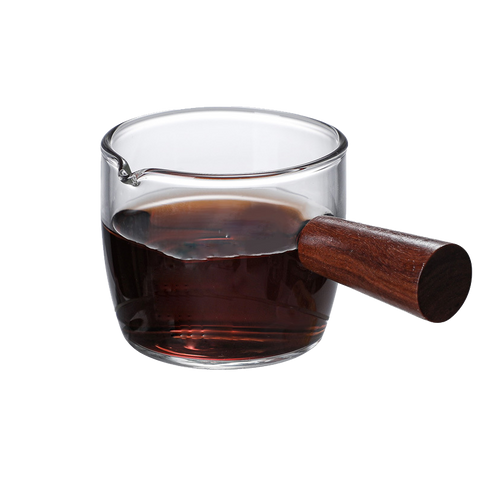 A clear glass coffee cup with a brown handle and measurement markings, filled with coffee.